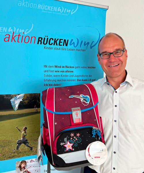 Dr. Kuhn übergibt symbolisch einen Rucksack für die Aktion Rückenwind, die Kinder aus sozial schwachen Familien unterstützt.